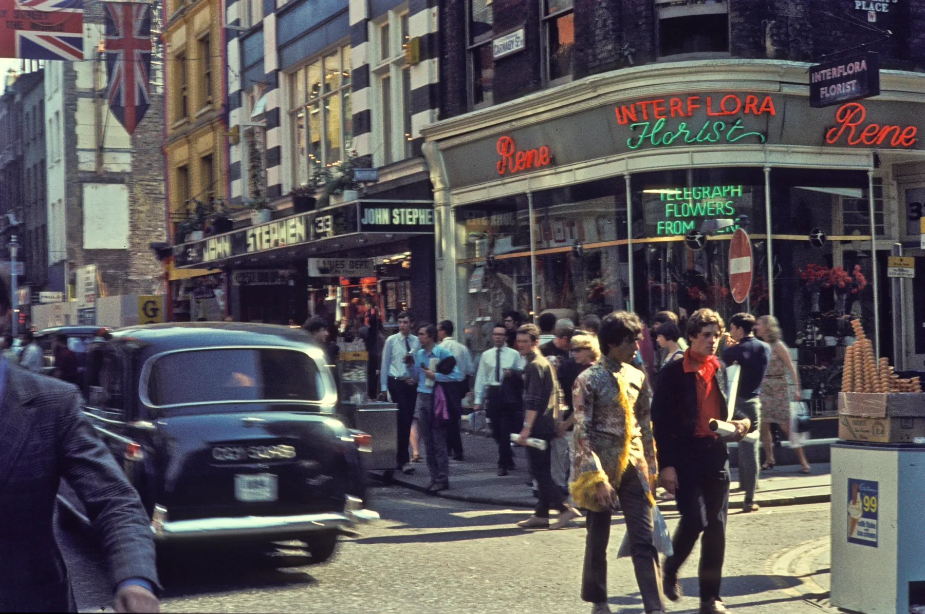 Járókelők, üzletek és egy fekete londoni taxi a Carnaby Streeten 1968-ban, H. Grobe korabeli színes fényképén.