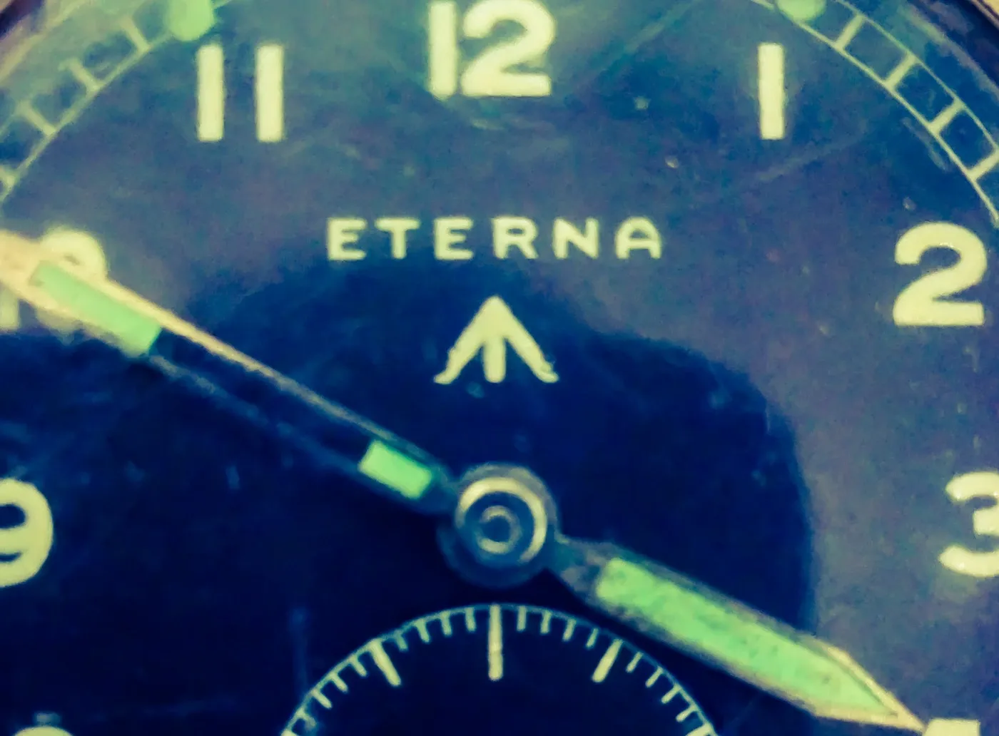 Eterna W.W.W. eredeti számlapfotójának részlete, Eterna felirattal, broad arrow jellel és patinás mutatókkal