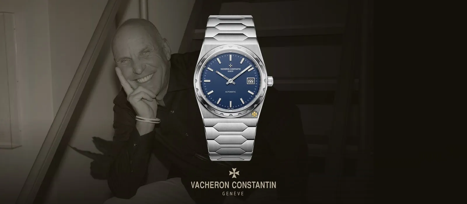 Jörg Hysek tervező mosolyogva egy lépcsőn, mellette a Vacheron Constantin 222 acél változata kék számlappal